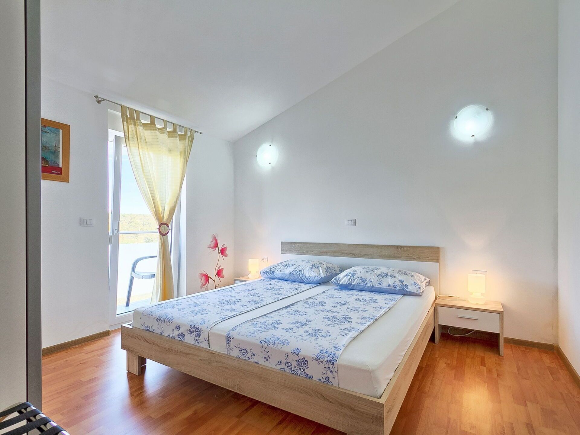 Ein Schlafzimmer mit einem hölzernen Bett, einem Nachttisch, einer Nachttischlampe und einem Fenster mit Vorhängen.