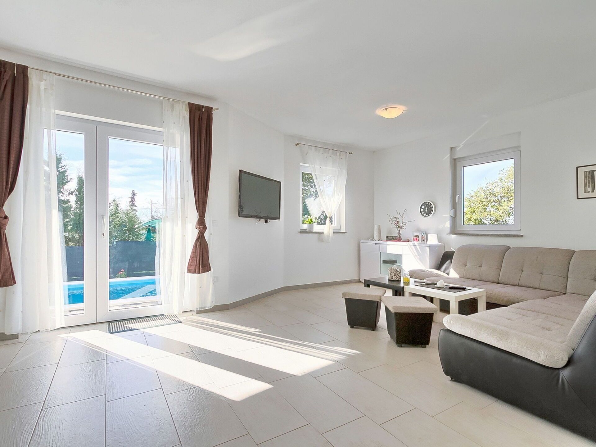Ein geräumiges Wohnzimmer mit großem Fenster, einer Couch, einem Couchtisch und einem Fernseher.