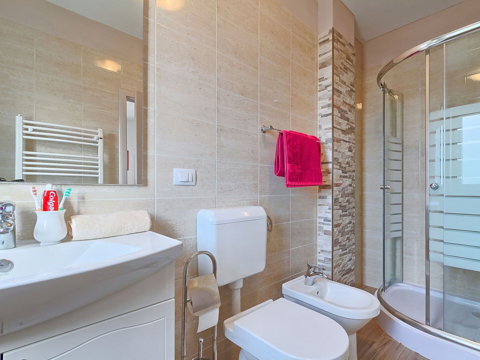 Een moderne badkamer met toilet, bidet, wastafel en een douchecabine met glazen wanden.