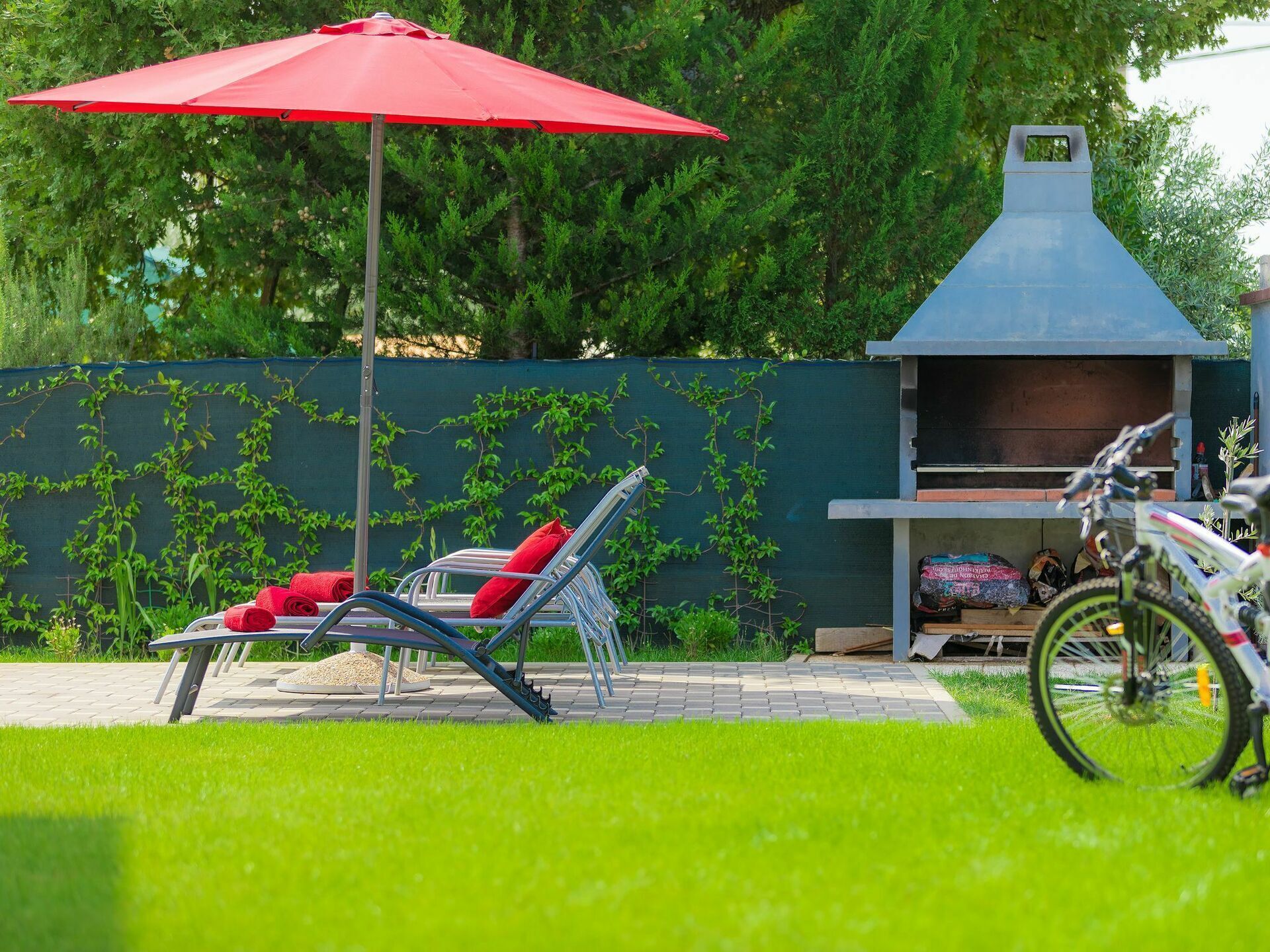 Un patio con una parrilla, un paraguas rojo y una silla con cojines rojos.