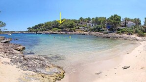 A beach with clear water, rocky shoreline, and houses in the background. - Paraiso sobre el Mar (Urbanización de la Torre, Porto Petro, Santanyí)
