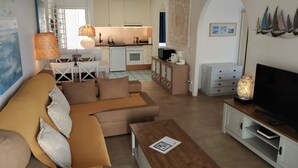 A modern living room with a sofa, coffee table, TV, and kitchen in the background. - La Paloma Blanca-WELCOMEPLAYABLANCA (Playa Blanca)
