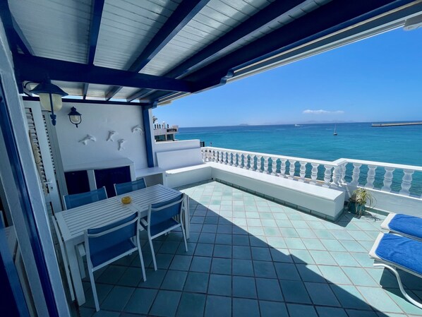 A covered outdoor seating area with a view of the sea, featuring a table and chairs, a sofa, and a railing. - La Paloma Blanca-WELCOMEPLAYABLANCA (Playa Blanca)