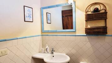 A bathroom with a white sink, a mirror, a framed picture, and a wicker basket with toiletries.