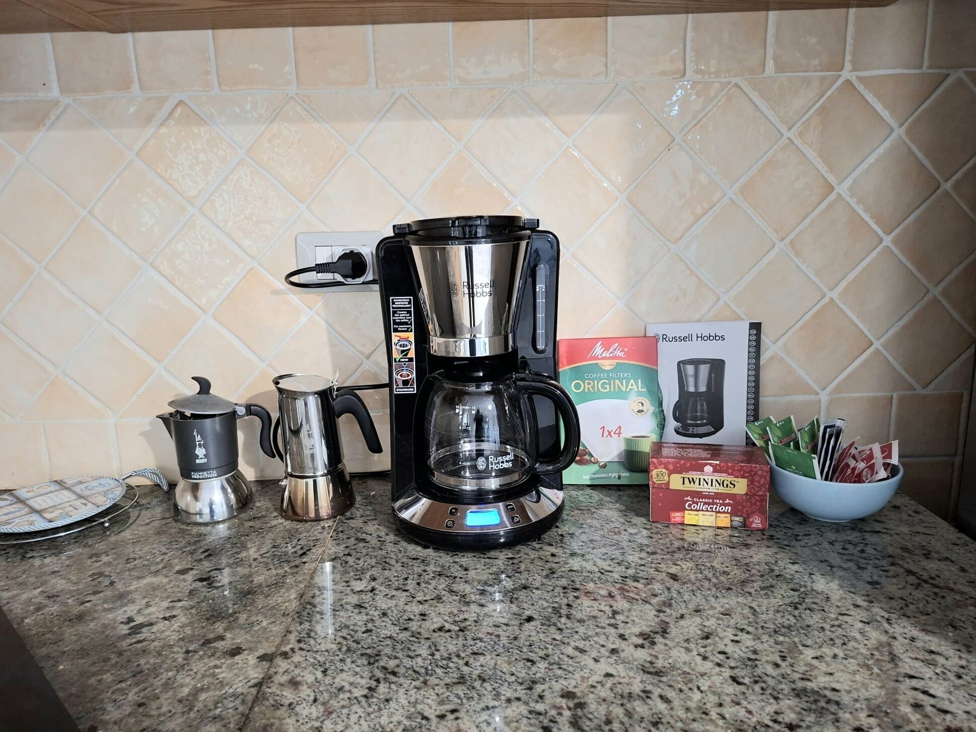 A kitchen counter with a coffee maker, a kettle, a coffee pot, and coffee filter boxes.