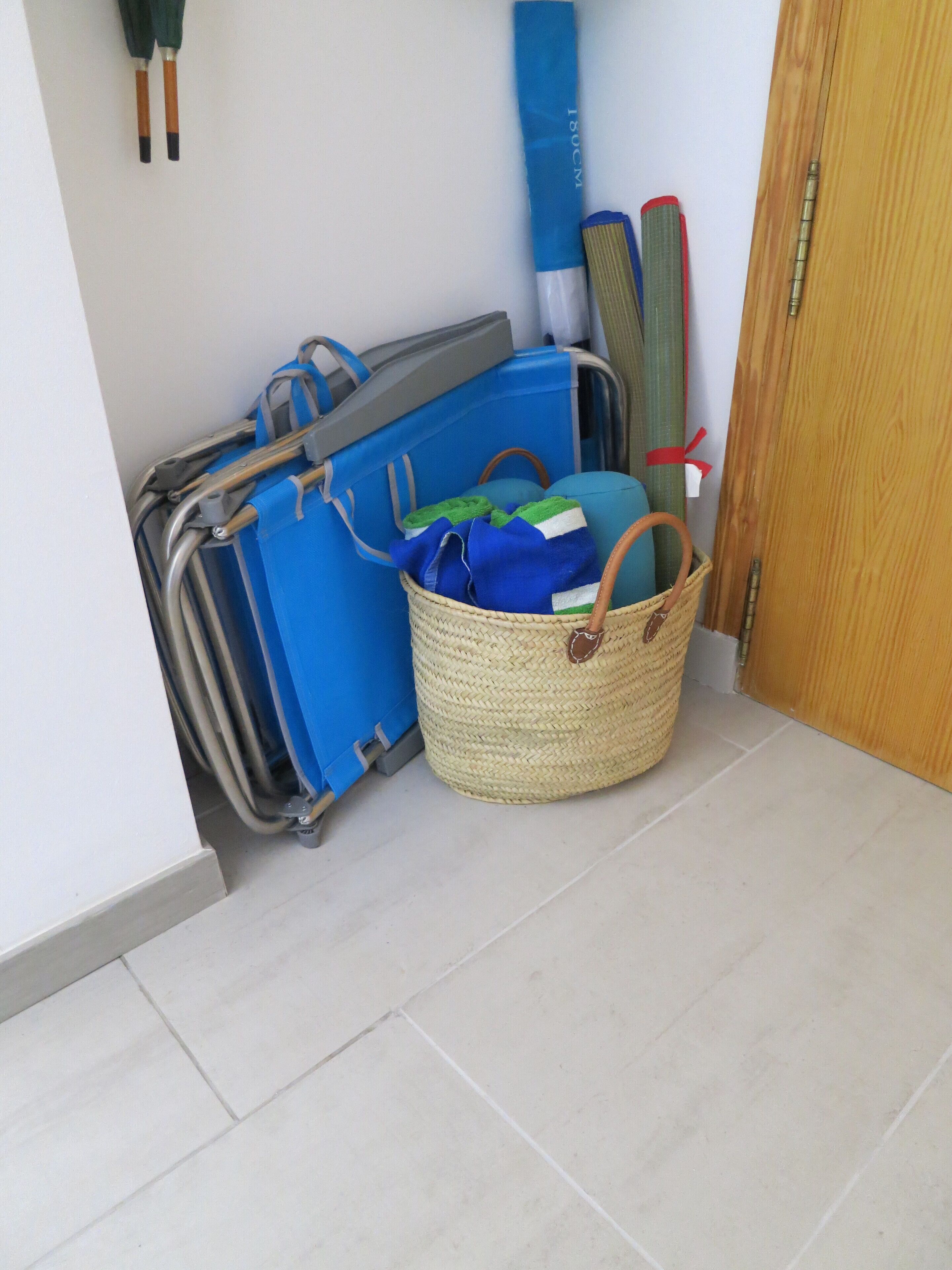 A room with a blue suitcase, a woven basket with clothes, and a door.