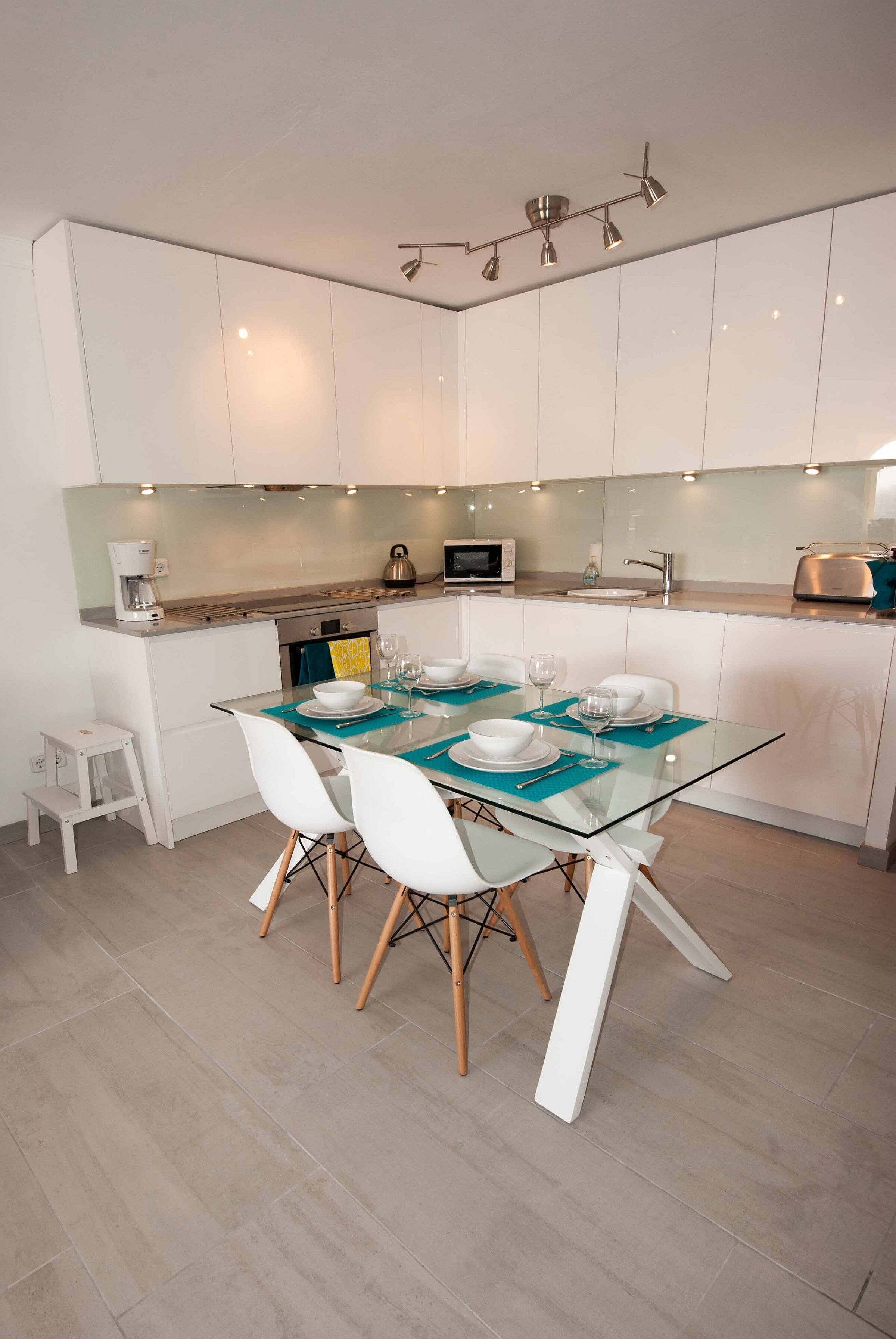 A modern kitchen with white cabinets, a glass dining table with white chairs, and a small island with a sink and microwave.