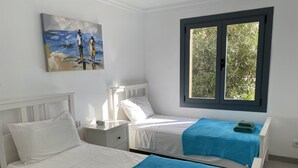 A room with two beds, a nightstand, a painting, and a window with a view of greenery.