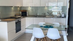 A modern kitchen with white cabinets, a glass dining table, and two white chairs.