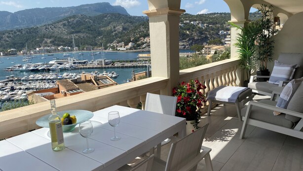 A terrace with a table set for two, overlooking a marina and mountains.
