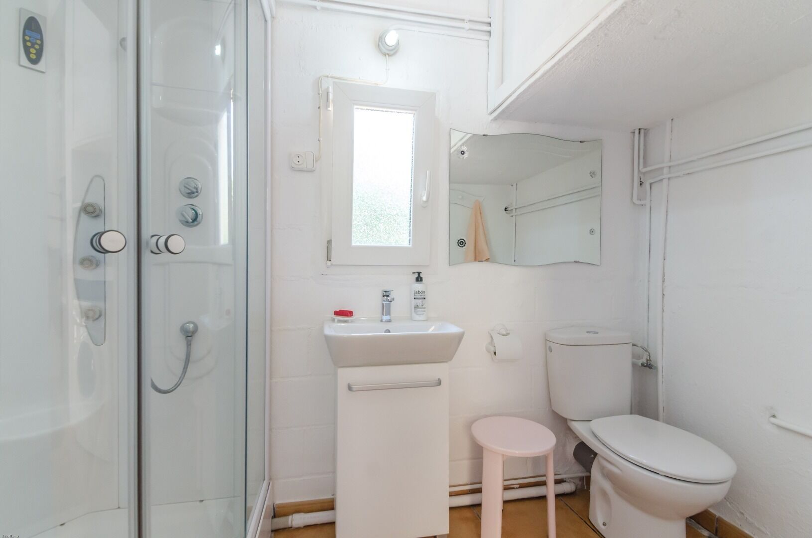 A bathroom with a glass shower enclosure, a white sink with a mirror above it, and a toilet.
