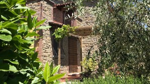 Un bâtiment en pierre doté d’une porte en bois et d’un balcon, entouré d’une végétation luxuriante.