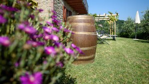 Un bâtiment en pierre avec une barrique en bois, une pergola, ainsi qu’une table et des chaises disposées dans un espace verdoyant.
