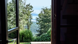 Une porte ouverte laisse entrevoir un espace extérieur verdoyant, avec une table et des chaises, entouré de végétation et offrant une vue sur la mer.