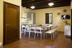 A dining area with a wooden table and white chairs, a kitchen with grey cabinets, and a TV mounted on the wall. - Eden Villas by the sea, adult pool, heated children's pool, private spa, 26 beds (Gorgo Lungo)