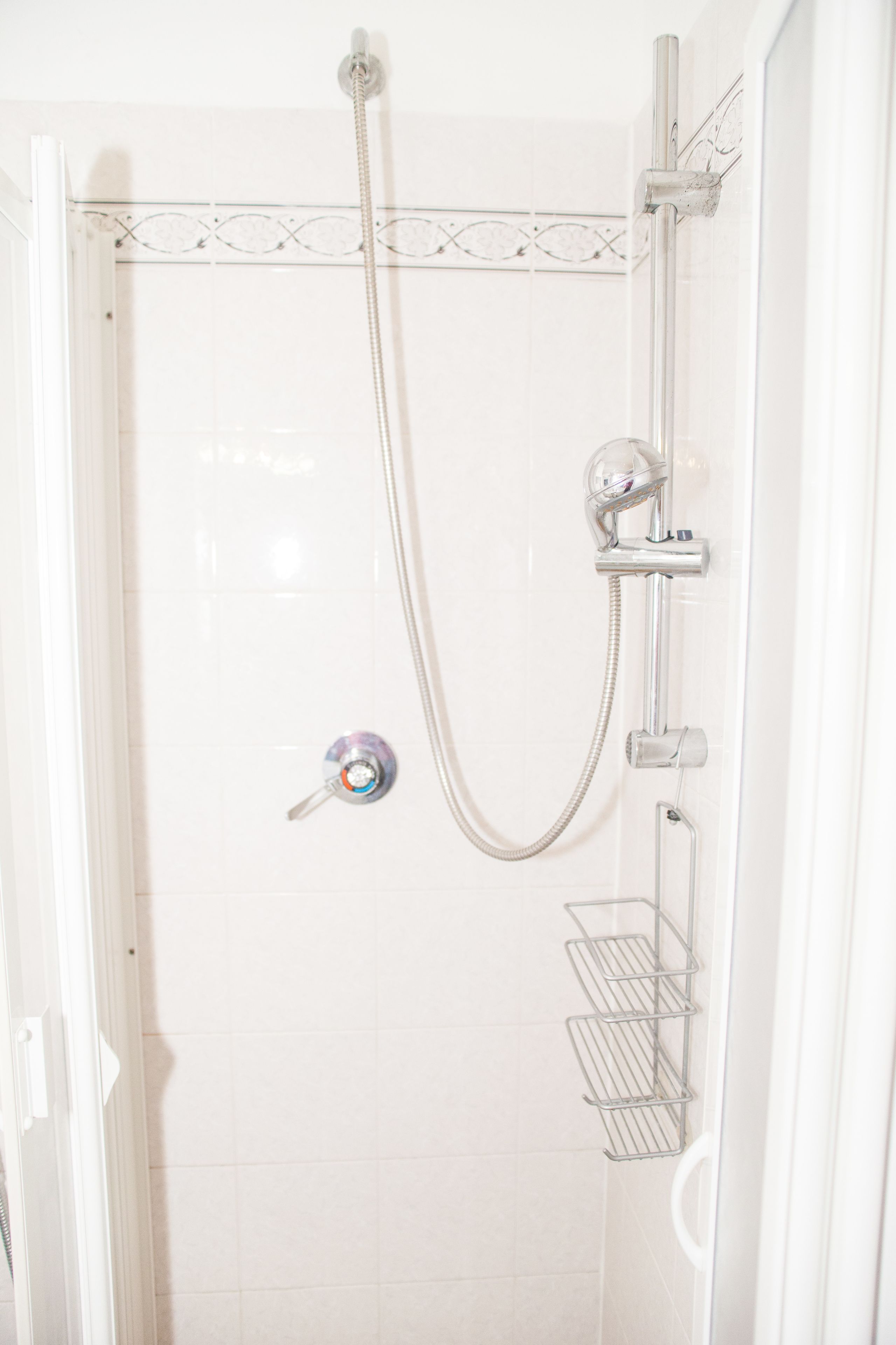 A shower with a handheld showerhead, a wall-mounted faucet, and a towel rack.