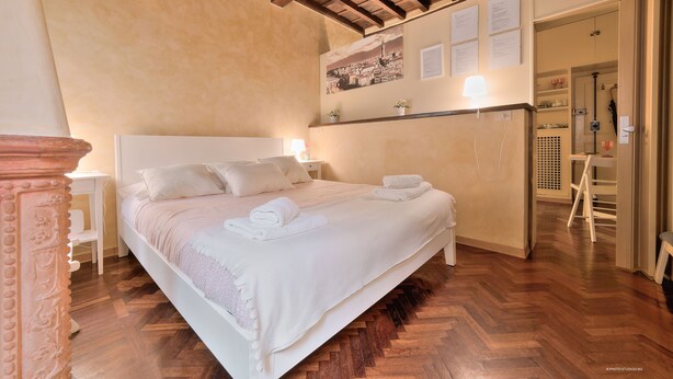 A neatly made bed with white linens and towels, a wooden herringbone floor, and a cityscape painting on the wall. - Wine Apartments Florence Trebbiano (Florence)
