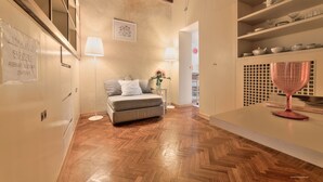 A cozy room with a herringbone wooden floor, a sofa, a table with a pink vase, and shelves with dishes and glasses. - Wine Apartments Florence Trebbiano (Florence)