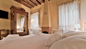 A hotel room with a large bed, a wooden dresser, a mirror, and a fireplace. - Wine Apartments Florence Trebbiano (Florence)