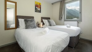 Ett hotellrum med två sängar, ett stort fönster med utsikt över bergen, en spegel och en affisch på väggen.
