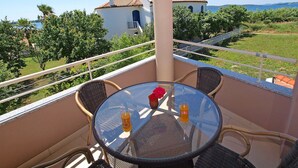 A balcony with a glass table, wicker chairs, and a view of a building and landscape.