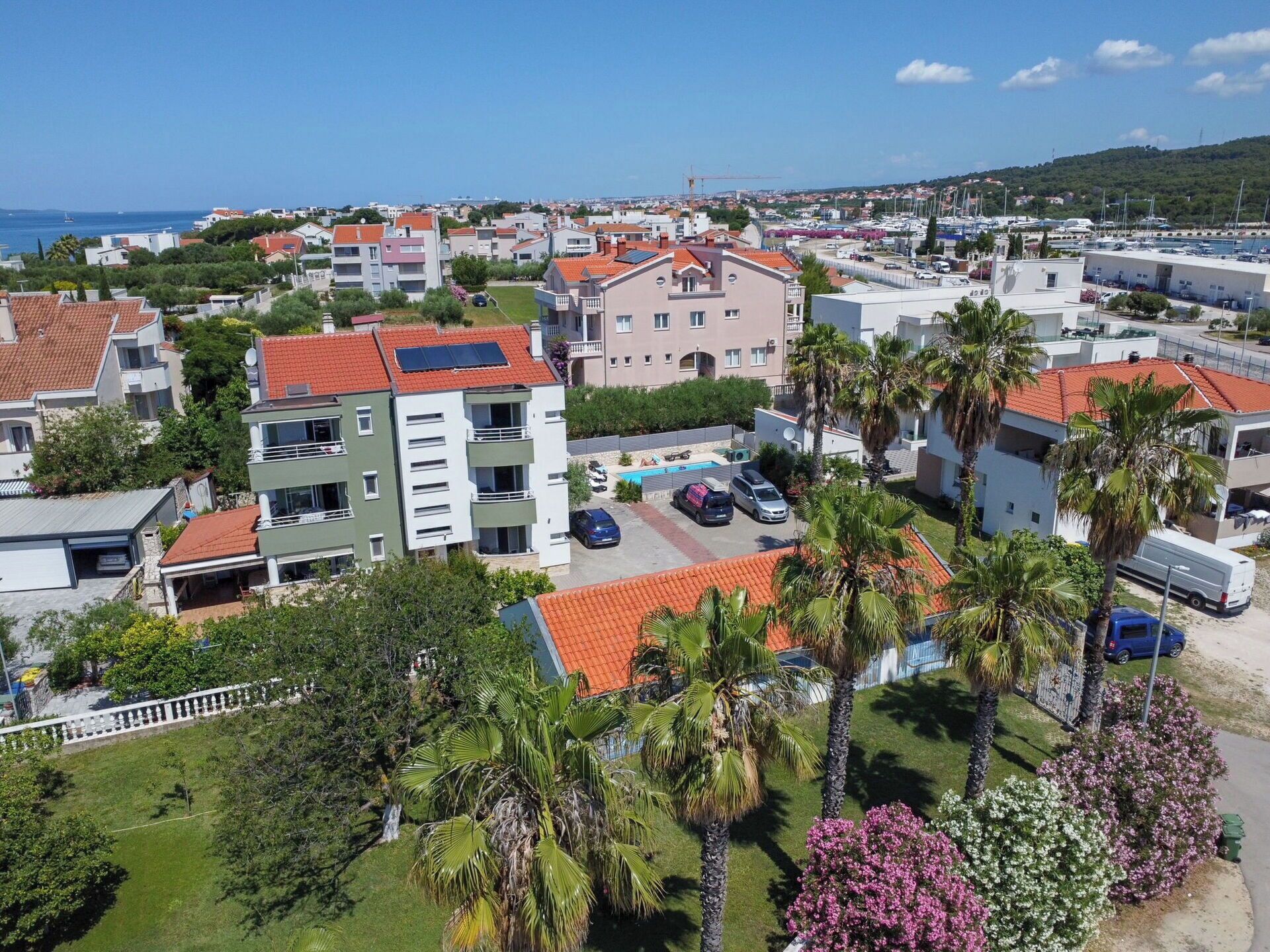 A residential area with modern buildings, a swimming pool, and a marina in the background.