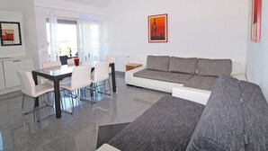 A modern living room with a grey sofa, white chairs, and a dining table.