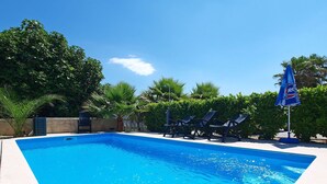 A swimming pool with clear blue water, surrounded by lounge chairs and palm trees.