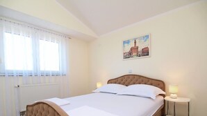 A neatly made bed with a tufted headboard, a bedside table with a lamp, and a painting of a cityscape on the wall.