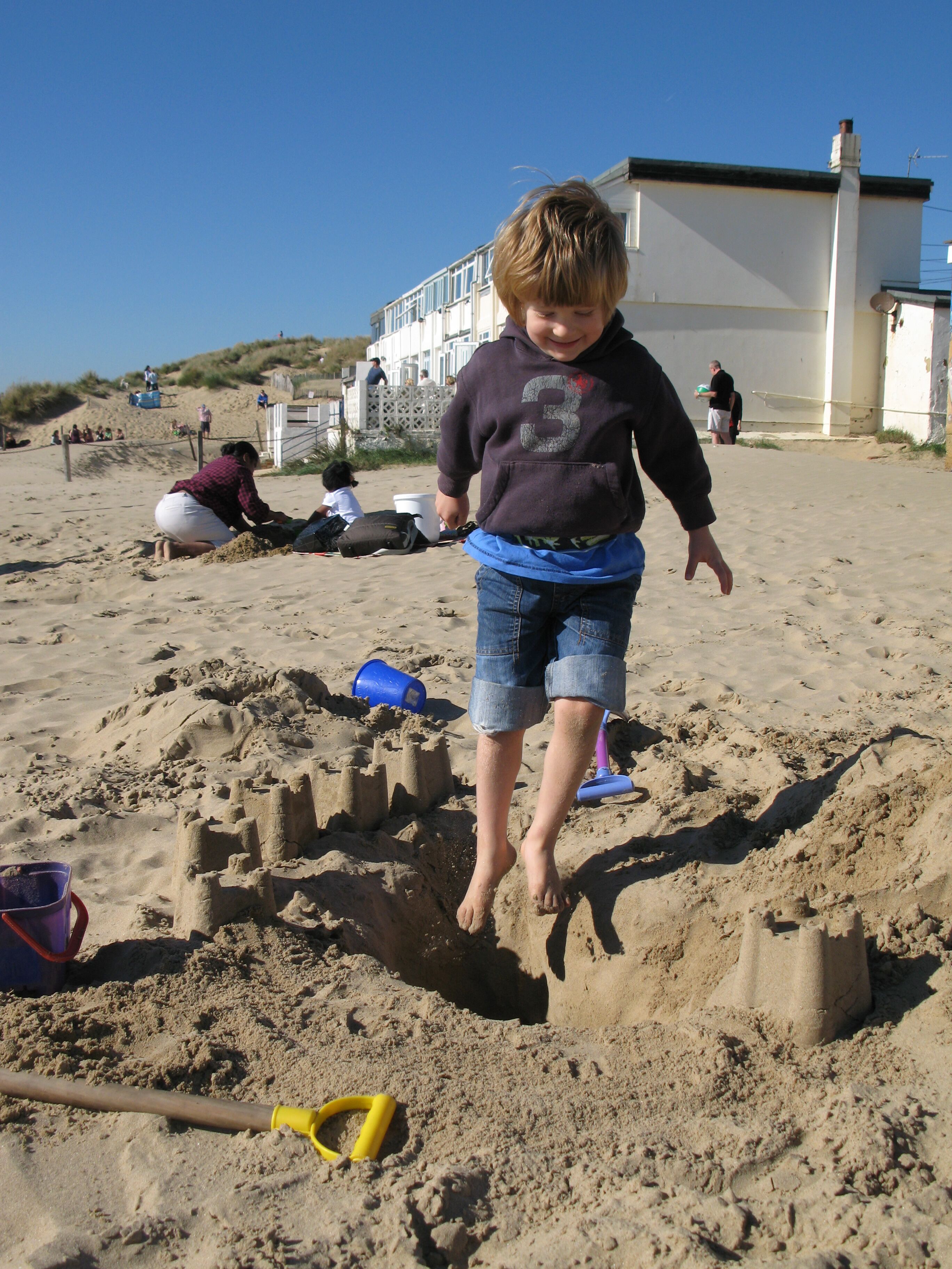 A child building a sandcastle on a sandy beach with a building in the background.