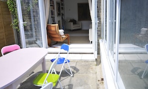 A patio area with a table and chairs, a sliding glass door leading to an interior space with a sofa and a painting.