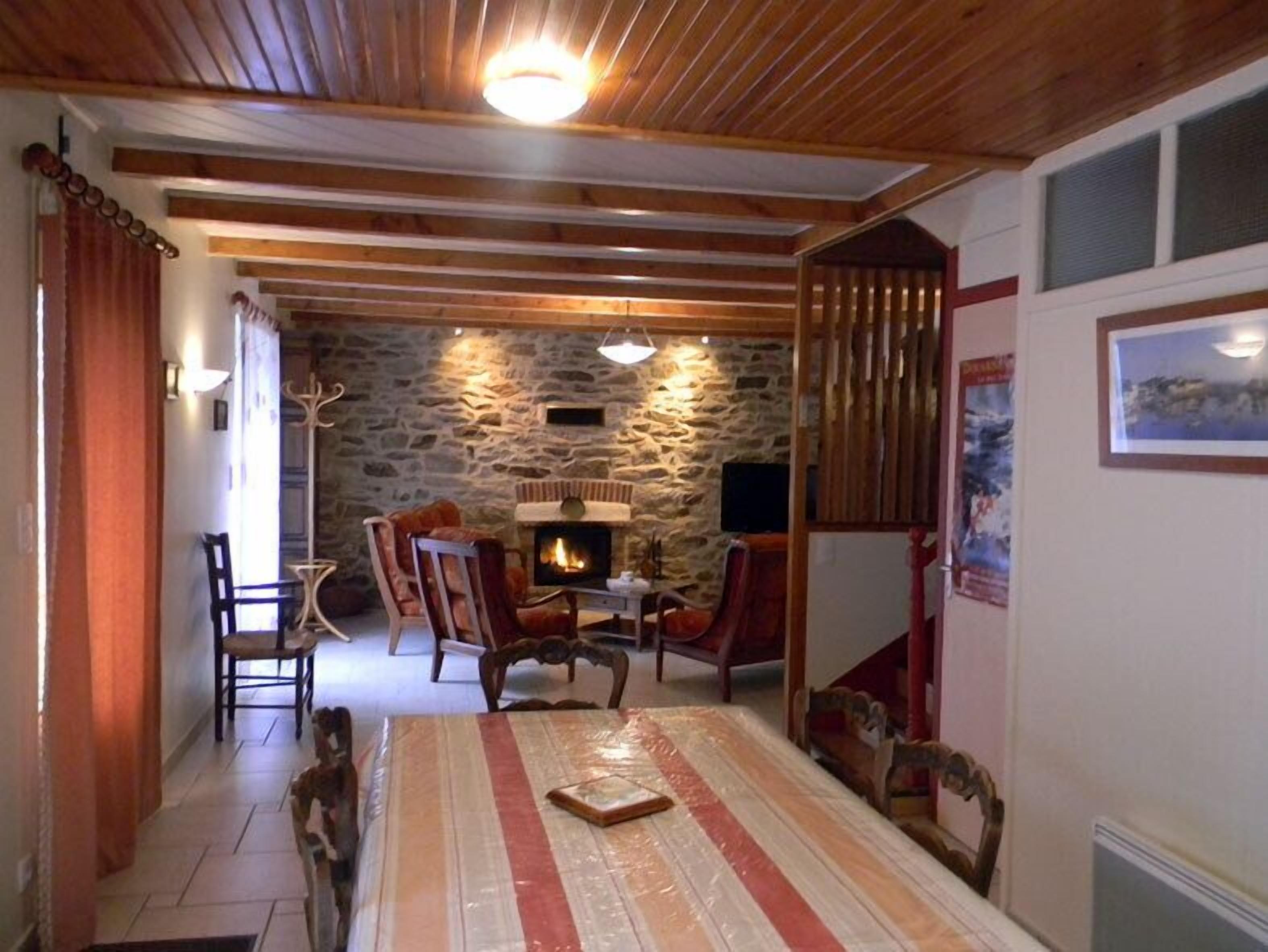 Une pièce chaleureuse avec un mur en pierre, un plafond en bois, une cheminée et un coin repas comprenant des chaises et une table.