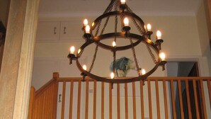 A wooden staircase with a railing leading to a second-floor balcony. A chandelier hangs from the ceiling, and a framed picture is visible on the wall. - House With Sea Views And Sunny Aspect (Thurlestone)
