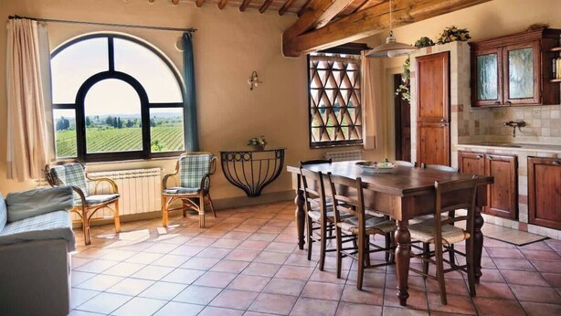 A rustic dining area with a large table and chairs, a view of vineyards through a window, and wooden cabinets.