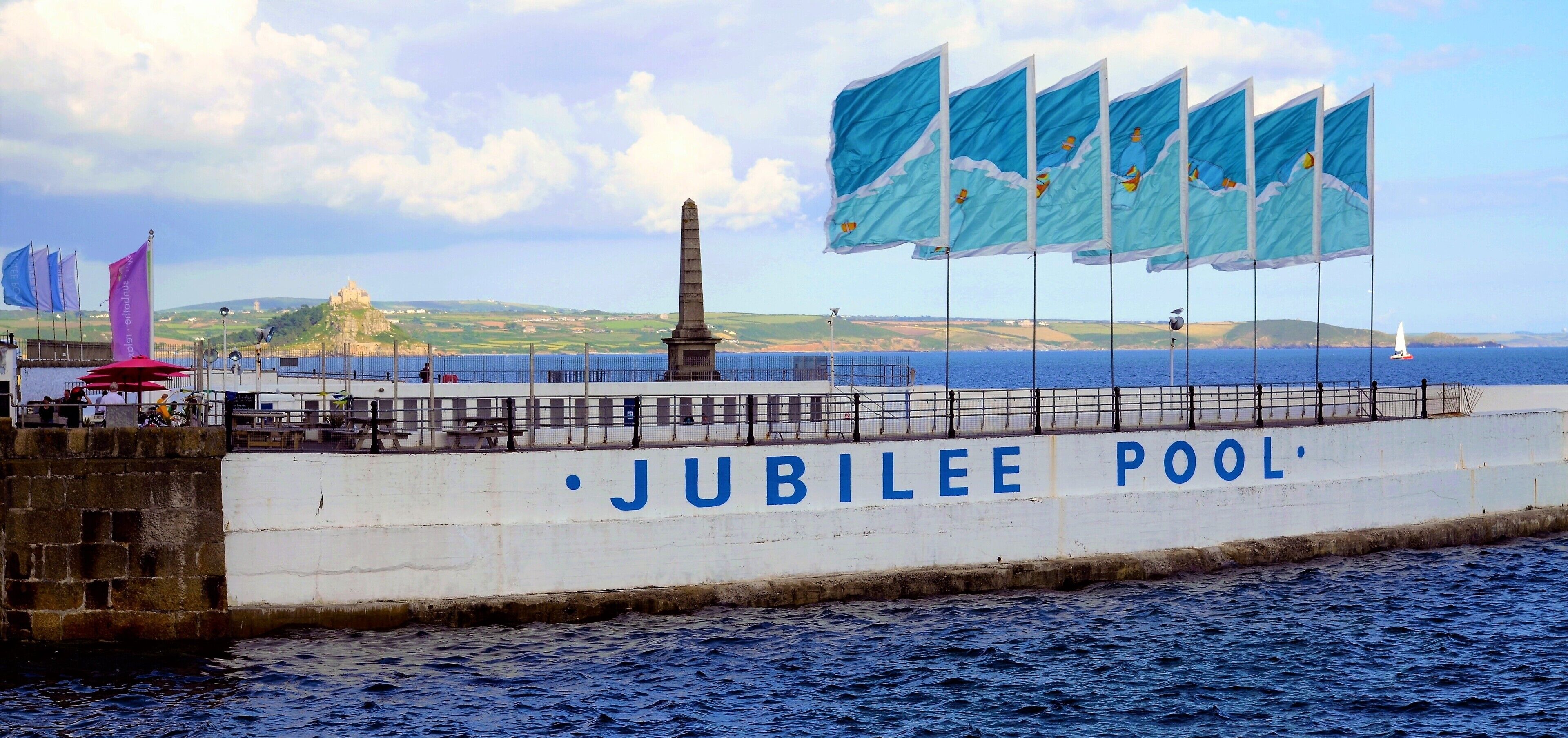 Eine Uferpromenade mit einem Denkmal und Flaggen, genannt 'Jubilee Pool'.