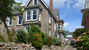 A stone house with multiple windows, a stone wall, and a garden with various plants and flowers. - Delightful quiet space, very close to the town & promenade.  (Penzance)
