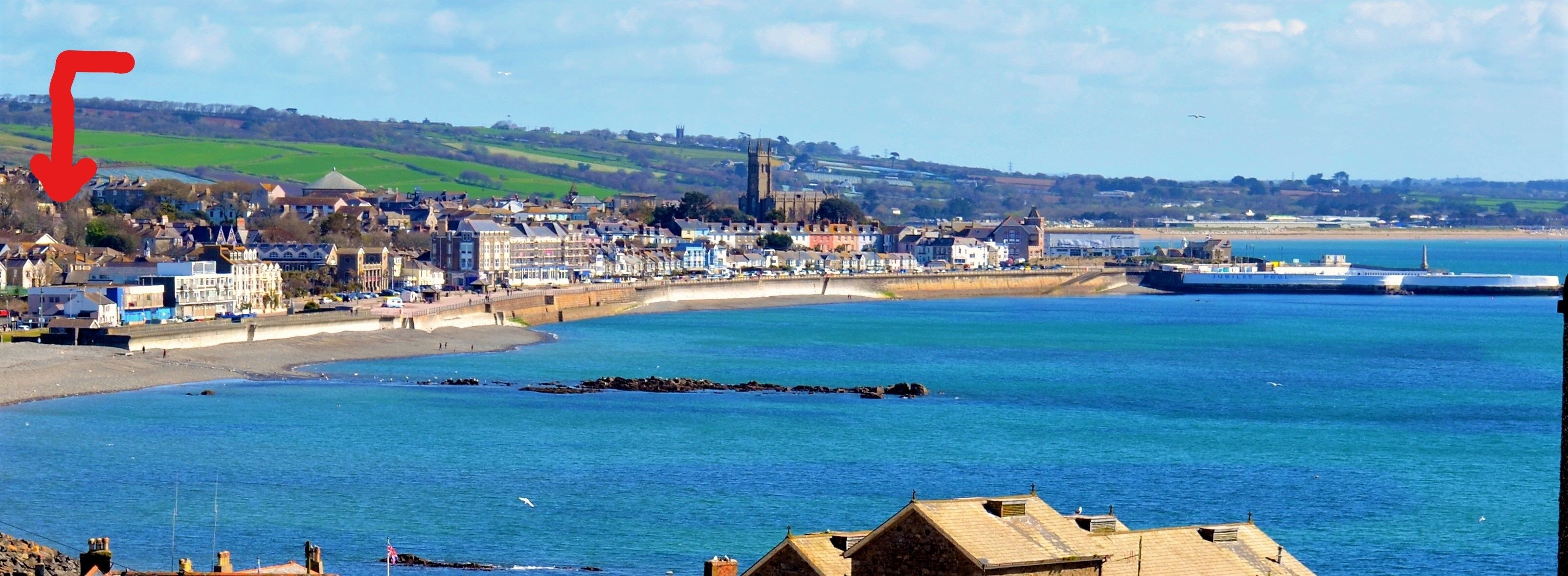 A coastal town with a sandy beach, a pier, and a large church in the background.