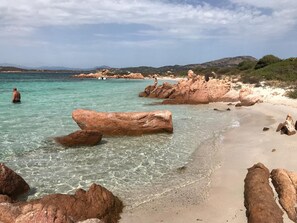A beach with clear turquoise water, large rocks, and a distant view of mountains.