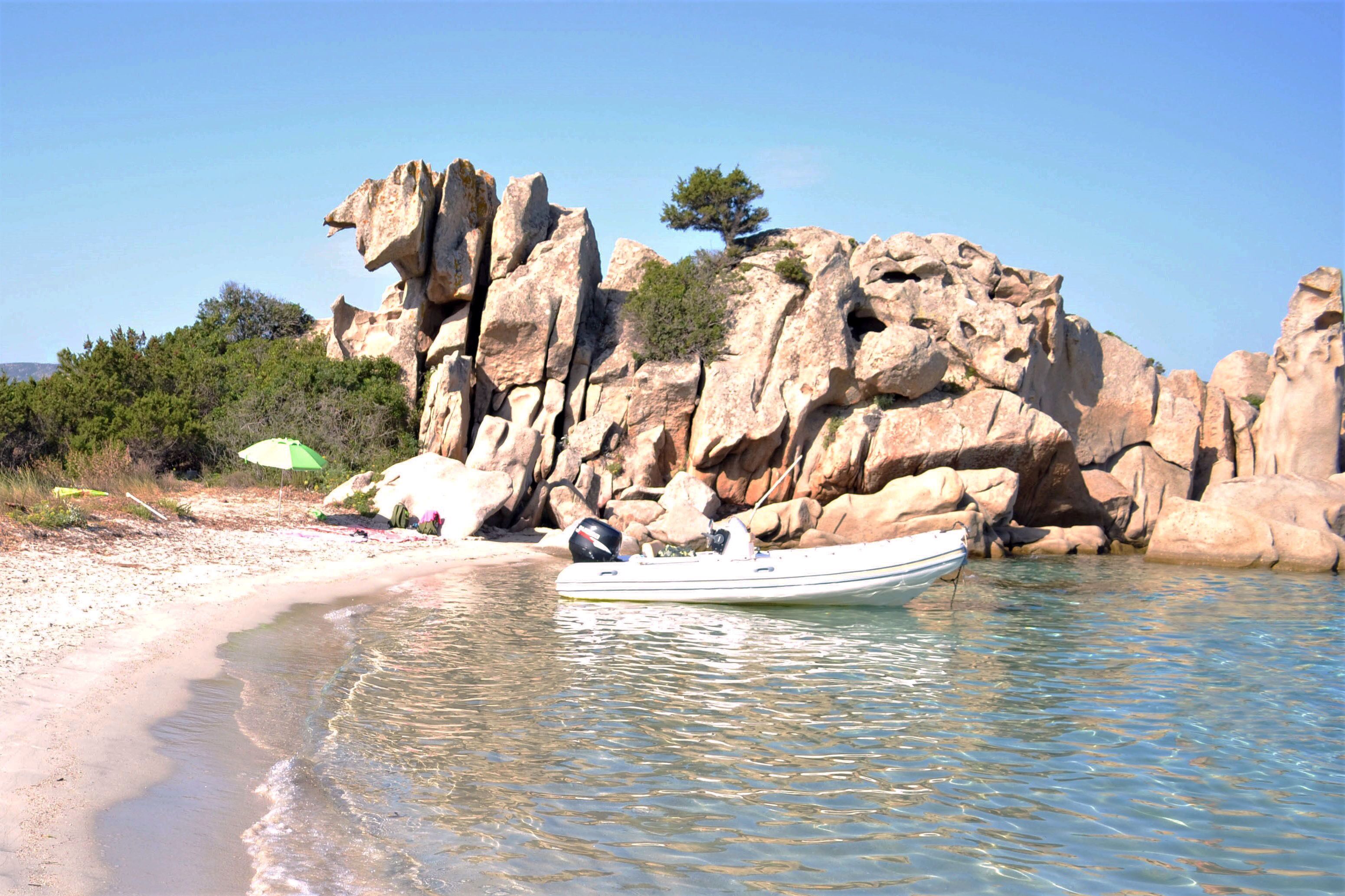 A boat on a clear beach with rocky cliffs in the background.