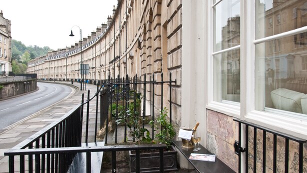 Une rue sinueuse bordée de bâtiments historiques, une rambarde en métal noir et un petit jardinier avec des plantes.