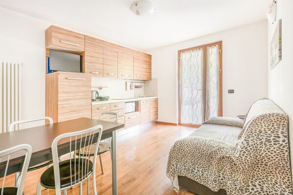 Un espacio habitable compacto con kitchenette, zona de comedor y cama con cubrefrío estampado de leopardo.
