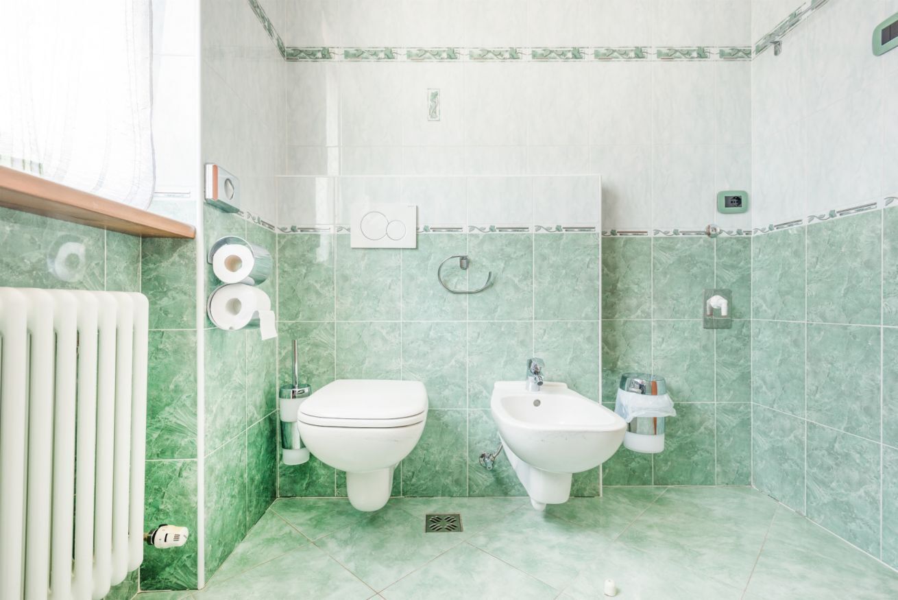A bathroom with two toilets, a bidet, and a radiator.
