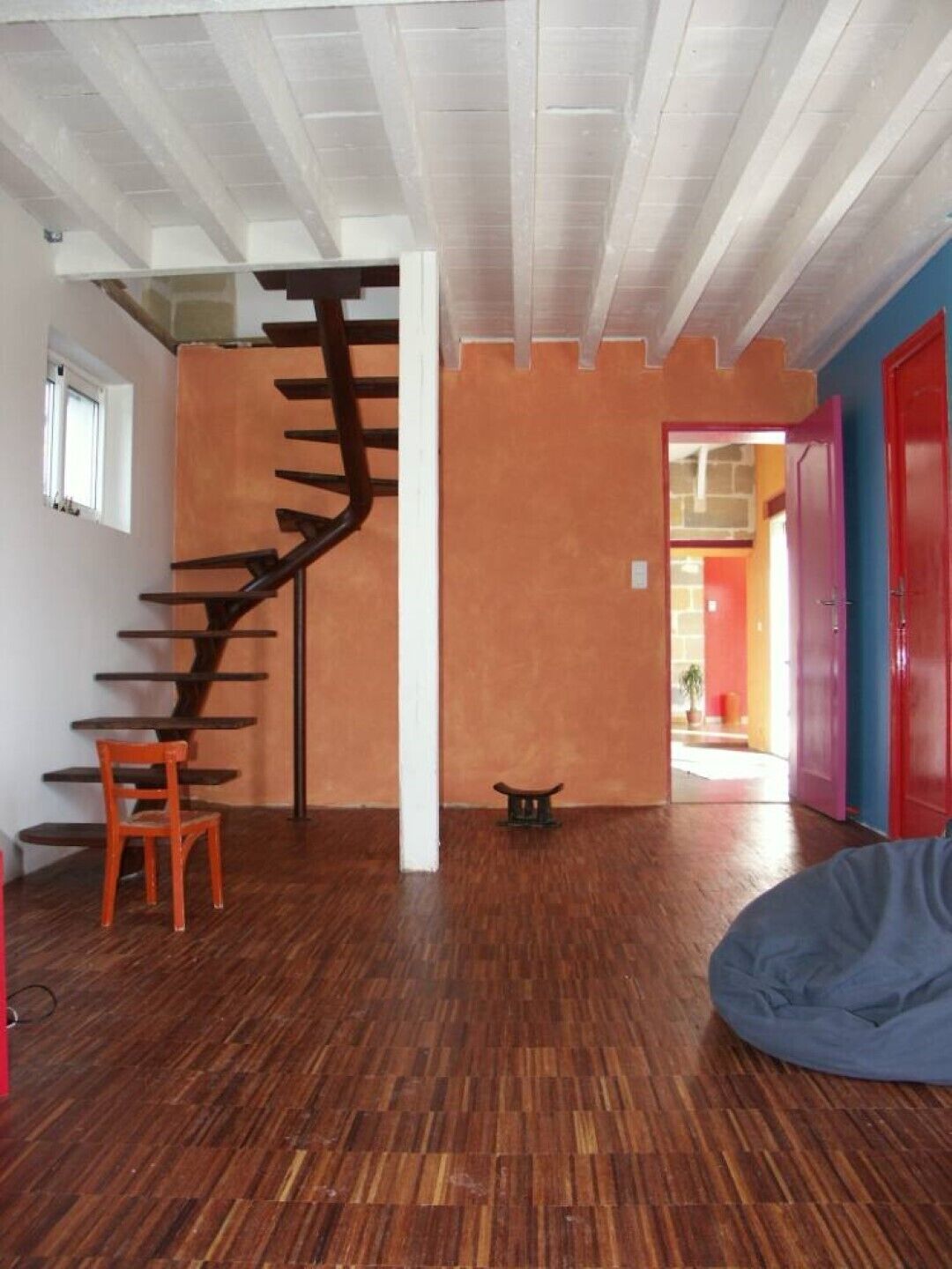 A room with a spiral staircase, a wooden floor, a red chair, and a blue bean bag.