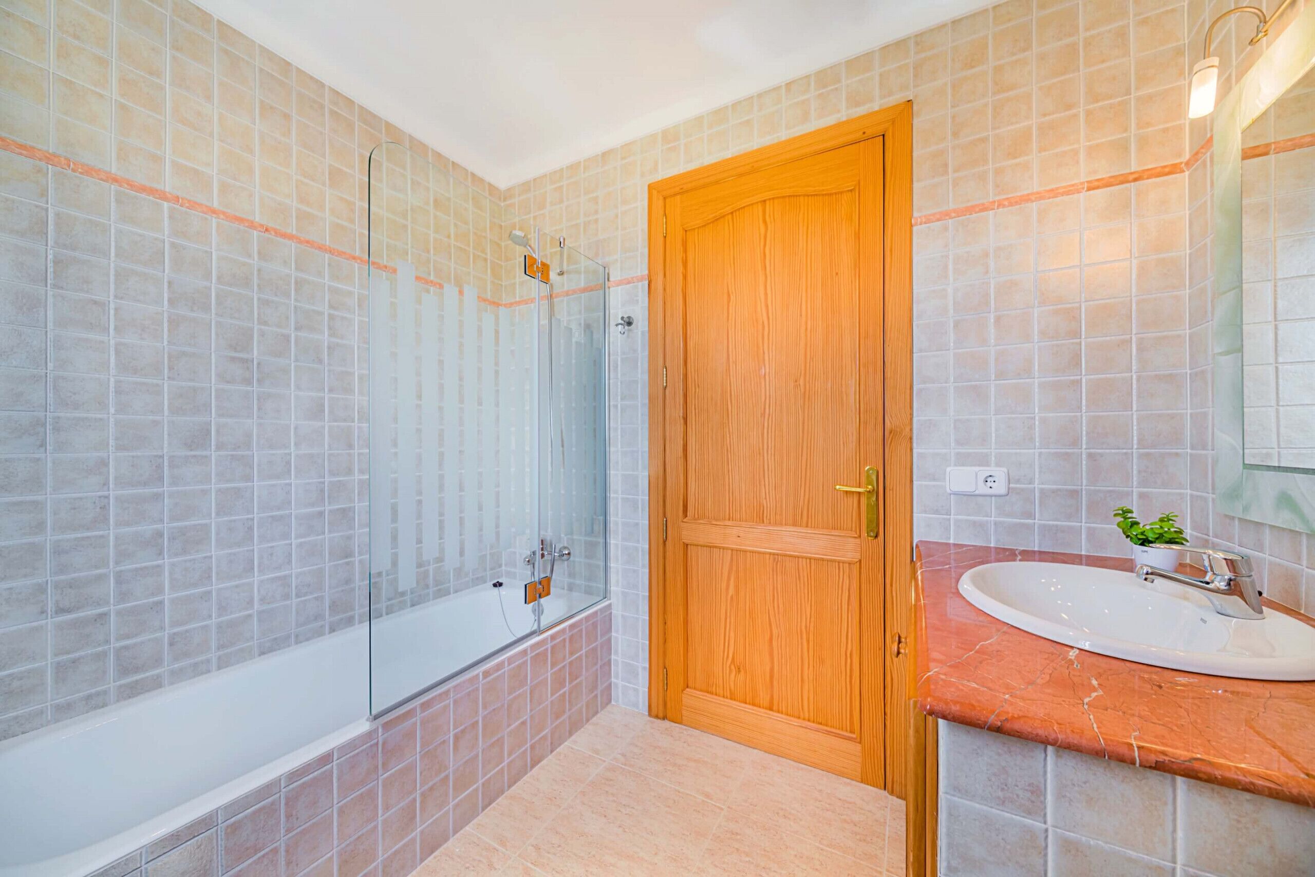 A bathroom with a glass-enclosed shower, a wooden door, and a marble sink.