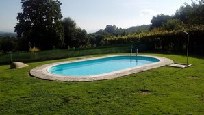 A rectangular swimming pool with a stone border, surrounded by a grassy lawn and a green fence. - Anxeliña House - HB001 (BOBORAS ,OURENSE)