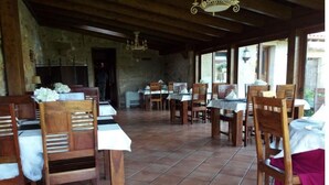 A rustic dining area with wooden tables and chairs, stone walls, and a tiled floor. - Anxeliña House - HB001 (BOBORAS ,OURENSE)