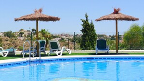 A swimming pool with lounge chairs and thatched umbrellas, surrounded by a fence and greenery. - Cosy apartment for 6 people with A/C, pool, WIFI, TV and terrace (Calpe)