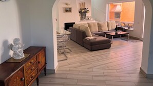 Un salon moderne avec un canapé d’angle, une table à manger en verre et un meuble en bois.