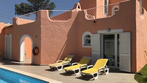 Un bâtiment doté d’une piscine, de chaises longues jaunes et d’une porte avec des volets.