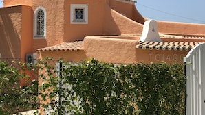 Un bâtiment aux murs en terre cuite, doté d’un toit en tuiles et d’une petite fenêtre ornée d’une grille décorative.
